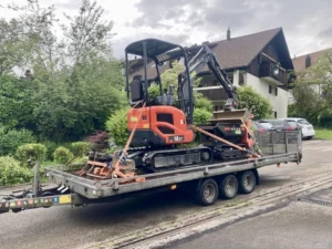 Minibagger Eurocomach 18ZT mit Dumper verladen auf Anhänger vor Wohnhaus – Tritten Baggervermietung liefert Maschinen direkt im Zürcher Oberland